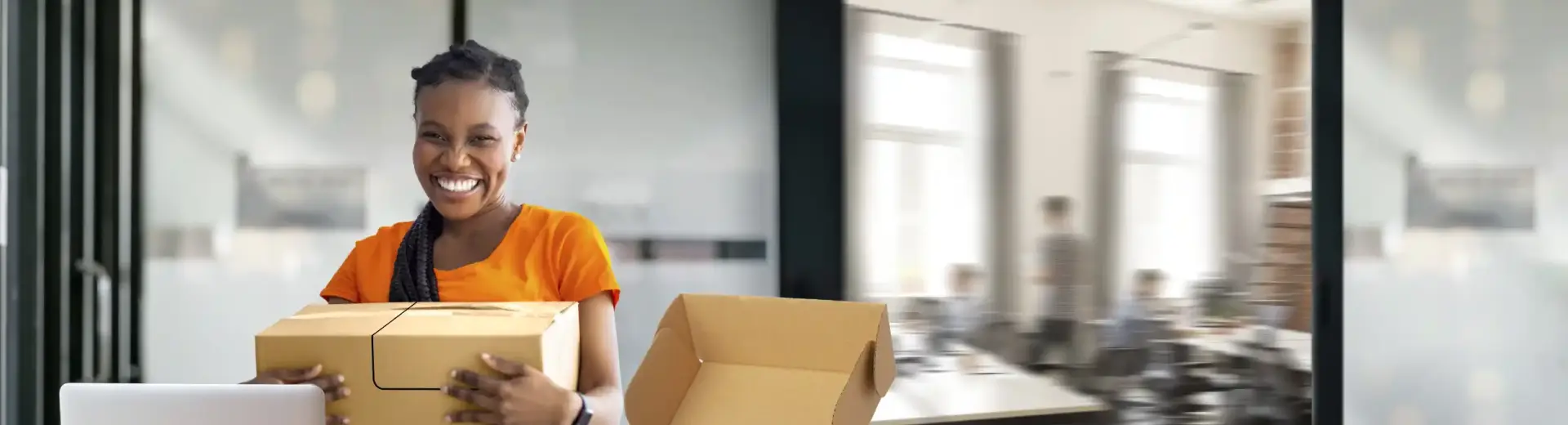 A smiling woman holding a GLS parcel in an office setting.